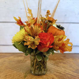 Autumn floral arrangement with orange roses and yellow blooms in a glass vase
