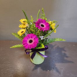 Pink and yellow daisy bouquet in a light green vase with a purple ribbon