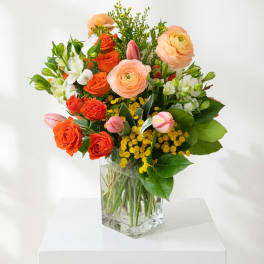 Mixed bouquet of orange and peach flowers in a clear glass vase
