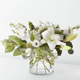 White lily bouquet in a clear glass vase with mixed greenery