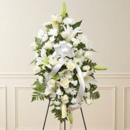 White floral standing spray with lilies, roses, and daisies on an easel