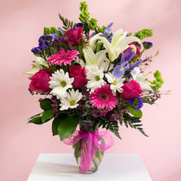 Mixed bouquet of pink roses, white lilies, and daisies in a glass vase