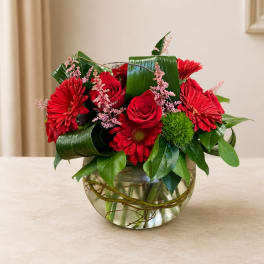 Red roses and gerbera daisies in a glass bowl vase