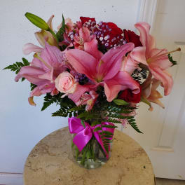 Pink lilies and roses in a glass vase with a magenta ribbon