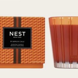Pumpkin chai scented candle in an orange glass tumbler beside its box