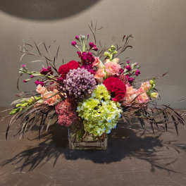 Mixed bouquet in a square glass vase with pink, purple, and green blooms