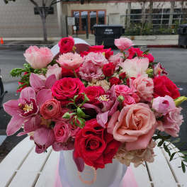 Pink and red mixed flower bouquet in a white hatbox