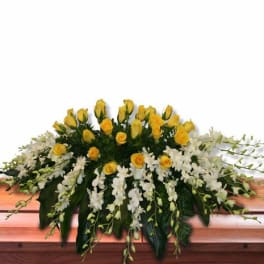 Yellow rose and white orchid casket spray arranged across a wooden casket