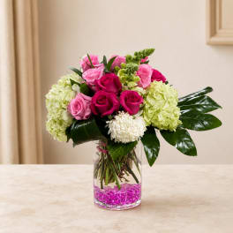 Pink and magenta roses with pale green hydrangeas in a clear glass vase