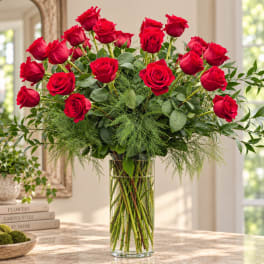 Red roses arranged in a tall clear glass vase with airy greenery