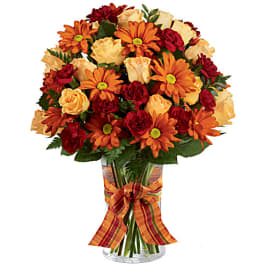 Bouquet of orange daisies, cream roses, and red carnations in a glass vase