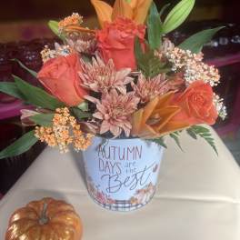 Autumn floral arrangement in a printed tin with orange roses and lilies