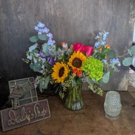 Mixed bouquet in a glass vase with sunflowers, roses, and blue flowers