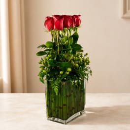 Red roses arranged in a tall glass vase with green accents