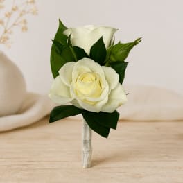 White rose boutonniere with dark green leaves and a wrapped stem