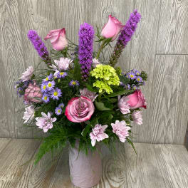 Pink roses and purple flowers arranged in a pink vase