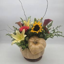 Fall floral arrangement in a pumpkin container with lilies, roses, and a sunflower