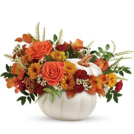 Orange and red floral arrangement in a white pumpkin vase