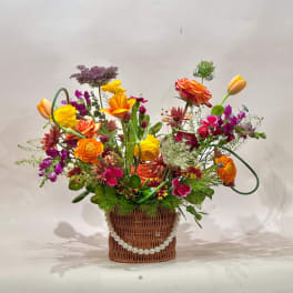 Colorful mixed flower arrangement in a wicker basket with a pearl garland