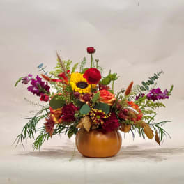 Mixed autumn bouquet in a pumpkin-shaped vase with sunflowers, roses, and purple blooms