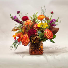 Mixed bouquet of orange, red, yellow, and purple flowers in an amber glass vase
