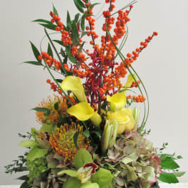 Tall floral arrangement with yellow calla lilies, orange berries, and hydrangeas in a white container