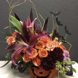 Halloween floral arrangement in a painted pumpkin container with bats and orange blooms