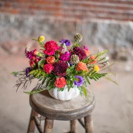 Colorful mixed bouquet in a white pumpkin-shaped vase on a wooden stool