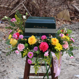 Colorful funeral spray around a dark urn with "In Loving Memory" text
