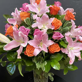 Pink lilies and orange roses arranged in a clear glass vase