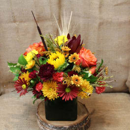Mixed bouquet of red, orange, and yellow flowers in a dark square vase