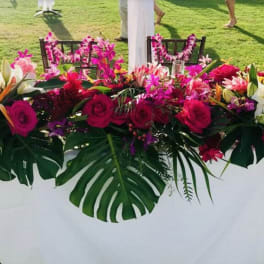 Long tropical floral centerpiece with pink roses and white lilies on a table