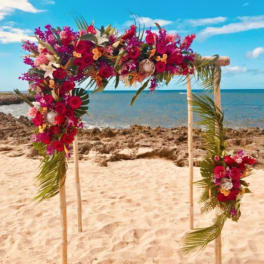 Floral arch with red, pink, and white flowers on a beach
