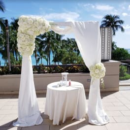White floral wedding arch with draped fabric and a small round table