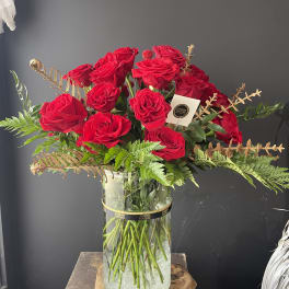 Red roses arranged in a clear glass vase with fern accents