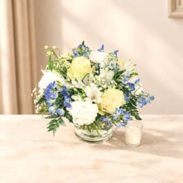 Blue and white flower arrangement in a clear glass bowl with a small candle beside it