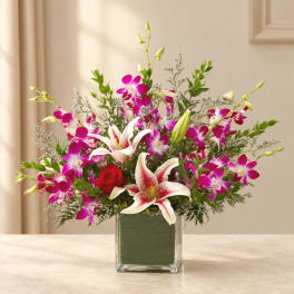 Bouquet of pink orchids, white lilies, and a red rose in a glass vase
