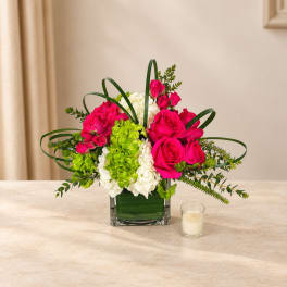 Pink roses and white hydrangeas in a square glass vase with a small candle nearby.