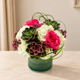 Pink roses and white hydrangeas arranged with succulents in a glass vase