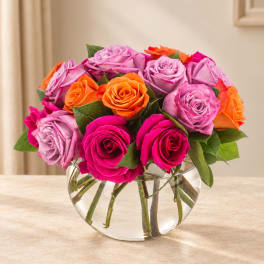 Bouquet of pink, lavender, and orange roses in a clear glass vase
