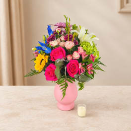 Colorful mixed bouquet in a pink vase with a small candle nearby