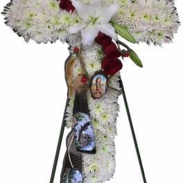White floral cross on a stand with red roses and a white lily