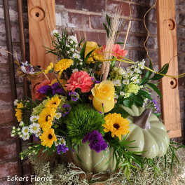 Mixed flower arrangement in a pumpkin-shaped container with yellow roses and daisies