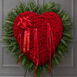 Heart-shaped red rose wreath with red ribbons on a stand