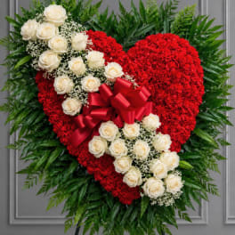 Heart-shaped red floral tribute with white roses and a red bow on an easel