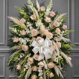 Standing floral spray with pale pink roses, white flowers, and a white bow
