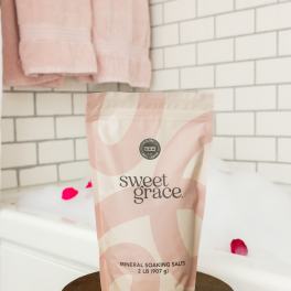 A pink and cream pouch of mineral soaking salts on a round stand.