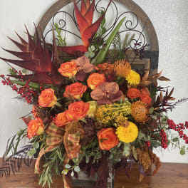 Mixed floral arrangement with orange roses and tropical blooms in a decorative container