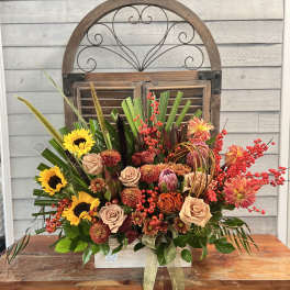 Large mixed floral arrangement with sunflowers, roses, and red berry accents in a wooden box