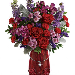 Red roses and purple mixed flowers in a red vase with a heart charm